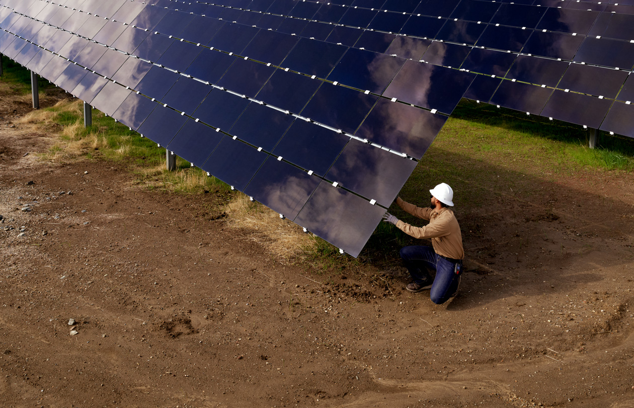 Une personne portant un casque de sécurité inspecte une installation photovoltaïque dans un champ