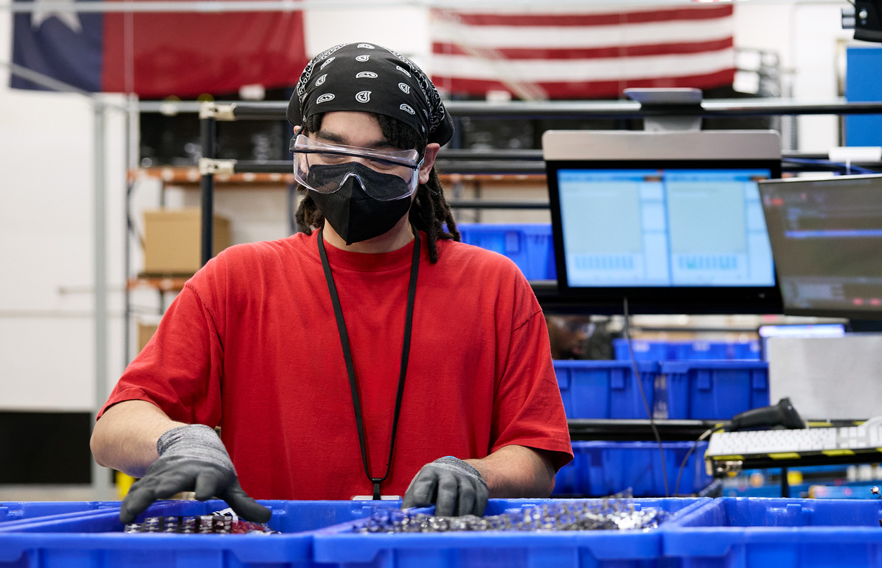 Une personne portant des gants, des lunettes et un masque manipule des matériaux dans une usine
